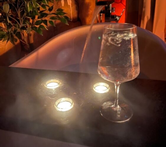Bath tub with running water and steam, tea light candles, and a glass of mineral water