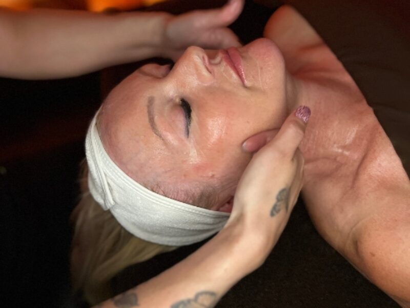 Hands on womans face, her eyes are closed, while getting an Esthetics facial